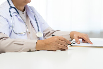 Fototapeta premium Female doctor sitting on the desk and working on patient clipboard data in hospital.