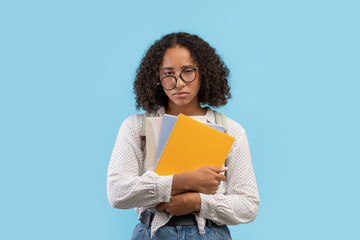 Sad black female student feeling tired, holding notebooks on blue studio background