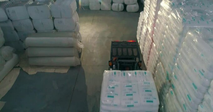 A forklift in a warehouse moves white bags. A forklift works in a warehouse. Forklift transports goods. White bags in a factory warehouse
