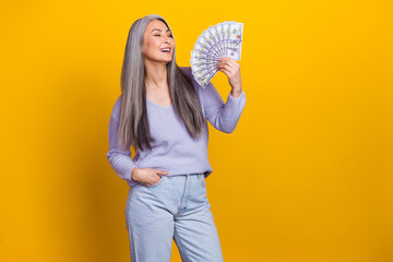 Photo of cheerful cool mature millionaire lady using money as fan feeling free isolated on yellow color background
