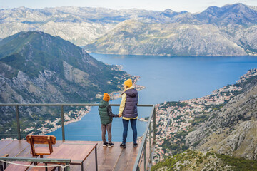 Fototapeta na wymiar Mother and son travellers enjoys the view of Kotor. Montenegro. Bay of Kotor, Gulf of Kotor, Boka Kotorska and walled old city. Travel with kids to Montenegro concept. Fortifications of Kotor is on