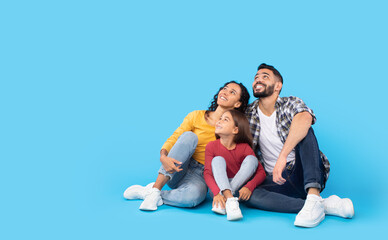 Happy Middle Eastern Family Sitting Looking Up Over Blue Background