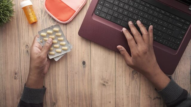  top view of hand holding blister packs and using laptop on table 