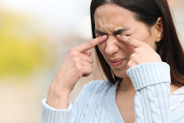 Woman scratching itchy eyes with her hands in a park