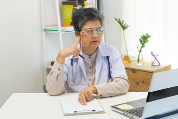 Fototapeta na wymiar Asian doctor woman using a laptop computer and writing something on paperwork or clipboard at hospital desk office, Healthcare medical concept.