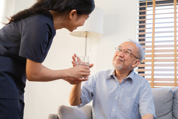 Obraz premium Asian young woman caregiver, carer supporting elderly, aged patient at home, drinking water after take medicine, cure or treatment disease of grandmother after retirement, help support.