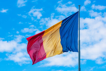Romania flag on flagpole. Flag waving in the wind on a blue sky with white cloudy