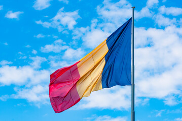 Romania flag on flagpole. Flag waving in the wind on a blue sky with white cloudy