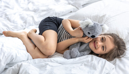 Obraz na płótnie Canvas Happy little girl with soft toy koala in bed.