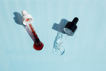 Open caps with dropper pipettes with serum. Blue background with daylight and the appearance of the texture of the liquid. Skincare products, natural cosmetic. Beauty concept for face and body care