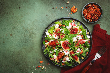 Delicious summer salad with figs, feta cheese, walnuts, arugula and sweet  jam dressing on rusty green table background, top view, negative space