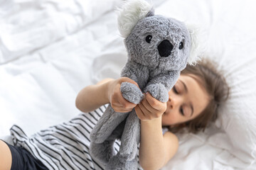 Happy little girl with soft toy koala in bed. © puhimec