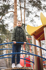 Happy teenager boy playing on kids playground. Outdoor activity. Portrait of joyful child in green jacket having fun outdoors. Carefree childhood.