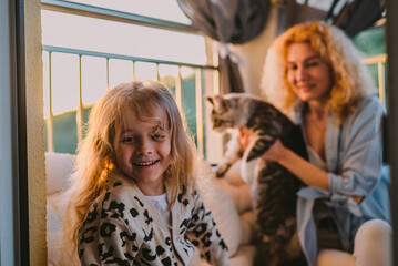 a little, happy girl, a child with a smile plays on a summer, spring vernada at home with mom and a...
