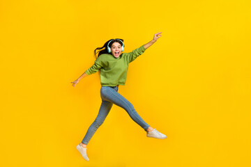 Full body profile side photo of young excited girl jump walk listen music earphones energetic isolated over yellow color background