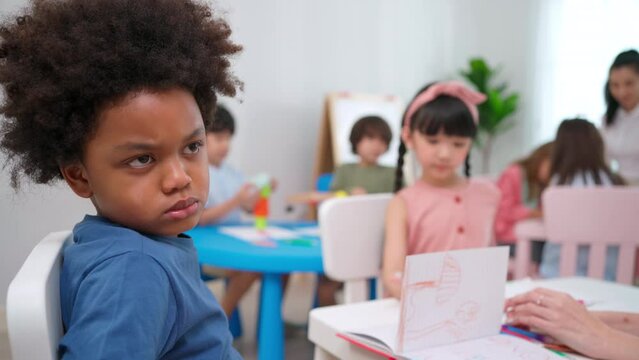 African American sitting in the kindergarten classroom during drawing or paining class. Feeling angry, boring and upset. Education and learning concept. Lifestyle in school. Lazy to study