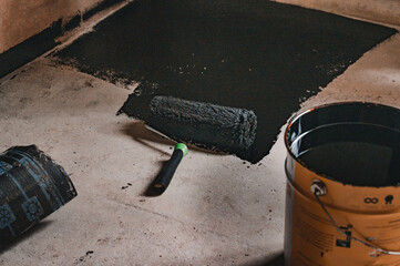 Applying hot resin to the floor for waterproofing, roller and bucket of resin.