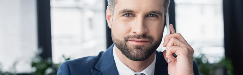 bearded businessman calling on smartphone in blurred office, banner.