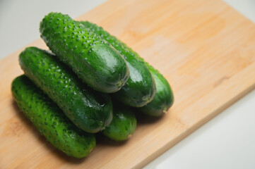 A pile of fresh small green cucumbers on a wooden cutting board on a white table