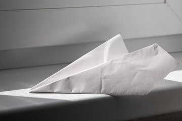 White paper plane lie on windowsill background in sun light. Origami hobby. Childhood is over. Old crumpled forgotten toy. Simple and fun game. Mockup design. Lockdown concept. Doesn't fly. Handmade