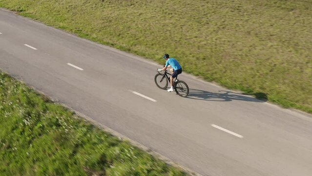 Side View Of A Male Professional Racing Bike Rider Cycling On A Paved Road On A Summer Sunny Day, Aerial Drone Shot.