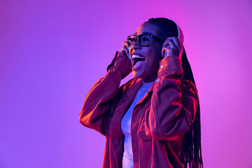 Music. Portrait of female fashion model in cotton shirt isolated on purple background in neon light. Concept of beauty, art, fashion, youth and emotions