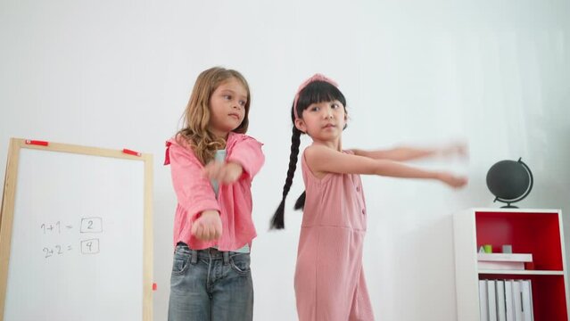 Two pretty girls standing in front of the classroom in the kindergarten school and show dancing to her friend. Learning, enjoy, education, playing concept. Feeling happy and fun.