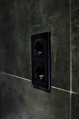 New black rosette on a ceramic tile of black color. Electrical outlet. Bathroom.