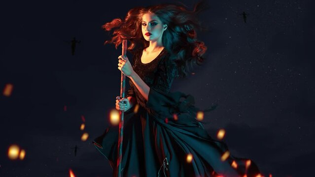 beautiful witch on a broomstick is flying to the sabbath. Young brunette woman in a dress and with a broom, rushing to a Halloween party, fire lighting, black background