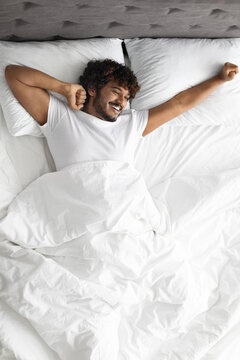 Happy hindu guy stretching in bed in the morning
