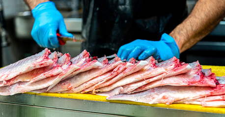A stall at the fish market. Men's hands in blue rubber gloves butcher sea fish