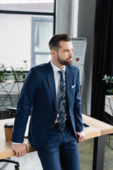 economist in suit standing at workplace in office and looking away.