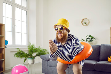 Funny crazy man with inflatable circle pretends to be swimming at home in living room. Absurd...