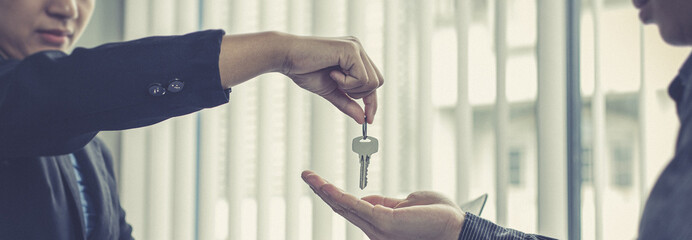 Sales manager or real estate agent holds the key handing it to the customer after signing the house purchase contract with home insurance, Trading of mortgages and insurance concept.