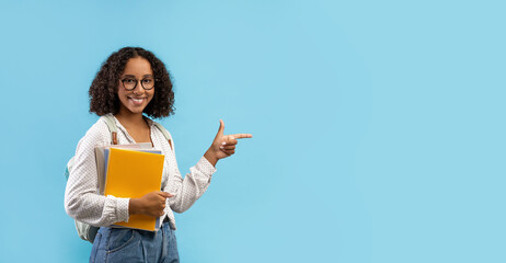 Beautiful black female student with backpack and notebooks pointing aside at empty space for your educational ad