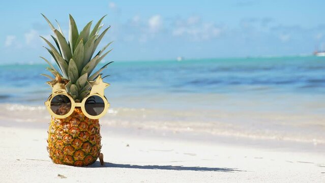 Pineapple in funny sunglasses on caribbean sandy beach. Tropical vacation