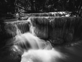 Scenic view of famous Erawan Waterfall. Closeup smooth flowing water tide in rainforest. Kanchanaburi, Thailand. Long exposure. Dramatic black and white.