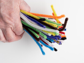 person clutching a bunch of sparkle and neon rainbow pipe cleaners on a white background