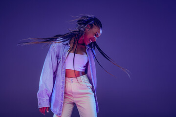 Emotional african girl in jeans and shirt dancing, having fun isolated on dark blue background....