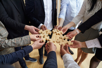 Team of business people holding wooden jigsaw puzzle pieces. Group of multiracial employees trying...