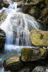 A mountain stream trickles down a mountainside in the sunlight and covers the rocks with white gout.