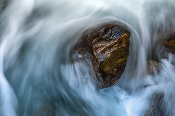 Water flows circularly around a rock photographed with motion blur.