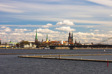 Plakat panorama of the city of riga, in the foreground is the daugava river, in the background is a blue sky and white clouds