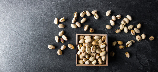 Obraz na płótnie Canvas Pistachios in a small plate with scattered nuts of almonds around a plate on a vintage wooden table as a background. Pistachio is a healthy vegetarian protein nutritious food. Natural nuts snacks.