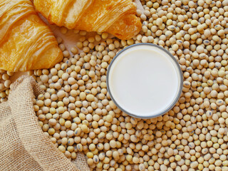 Cup of soy milk on lots of soy beans with sack of soy beans and two pieces of croissants 