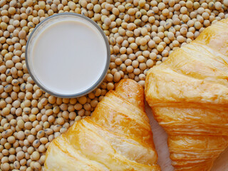A glass of soy milk on lots of soy beans with s two pieces of delicious croissants 