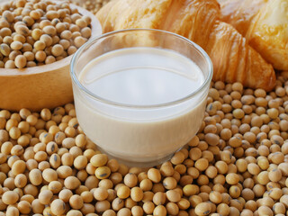 A cup of soy milk on lots of soy beans and cup of soy beans and croissants 