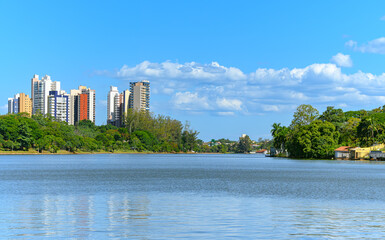 Landscape of Igapo lake, Londrina - PR, Brazil. Beautiful city lake, with trees around the shore and the city buildings on background, on a blue sky day.