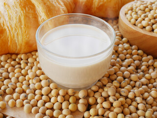 Glass of hot soy milk on lots of soy beans with wooden bowl of soy beans with some croissants 