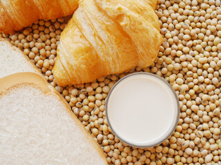 Glass of hot soy milk on lots of soy beans and some breads and some croissants